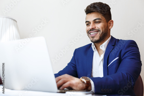 Cheerful young businessman working with laptop in hotel room
