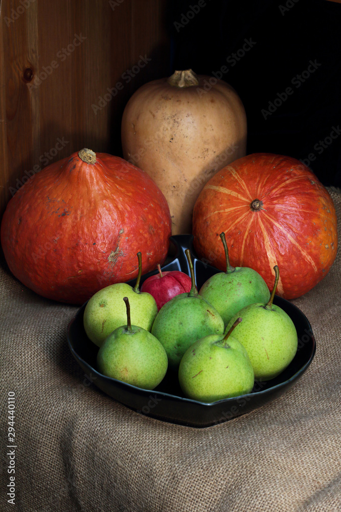 Still life orange yellow pumpkins butternut squash and red green pears, autumn farm harvest on retro canvas and black plate. Autumn fall atmospheric dark harvest still life on black background