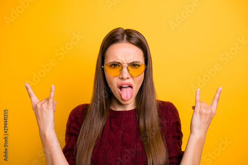 Close up photo of cheerful girl with eyeglasses eyewear showing horns sign wearing burgundy jumper isolated over yellow background