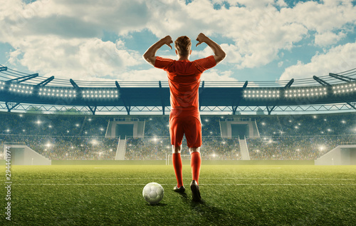 Professional soccer player in sports uniform with a ball on a field with tribunes, green grass and spectators. Blue cloudy sky © TandemBranding