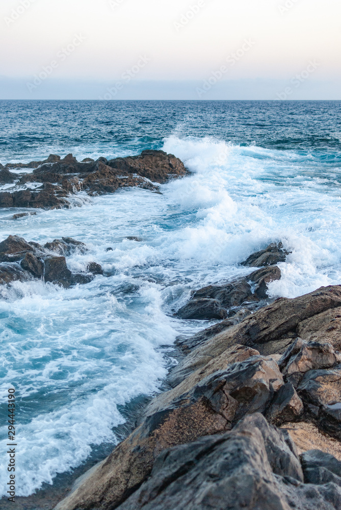 waves of the ocean are breaking from the rocky coast (vertical photo)