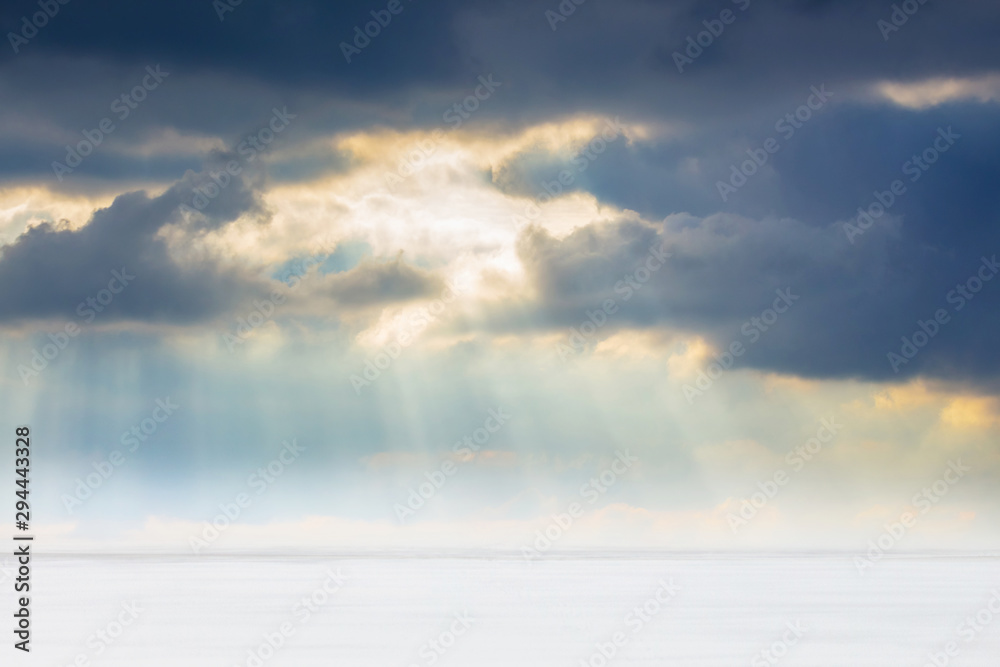 The rays of the sun penetrate the dark clouds over a white snowy field_
