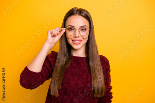 Portrait of charming lady touching her specs smiling wearing marsala pullover isolated over yellow background