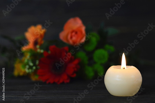 Condolence card with burning candle and flowers on dark background