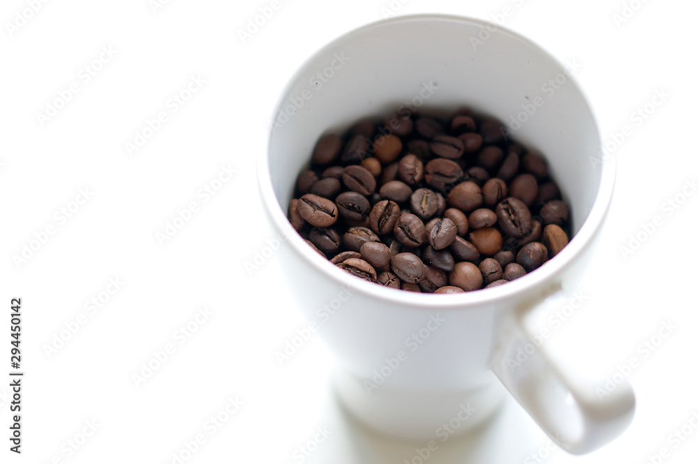 Grains of coffee in a white cup on a white background. Horizontal frame. Grains of coffee in a white cup on a white background. Horizontal frame.