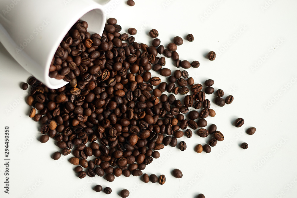 A scattering of aromatic coffee on a white background with a cup. A scattering of aromatic coffee on a white background with a cup.