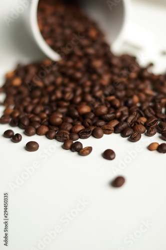 Coffee beans on a white background are beautifully scattered from a white cup.