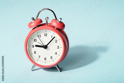 Red alarm clock with shadow on blue background. Seven minutes past nine on the clock photo
