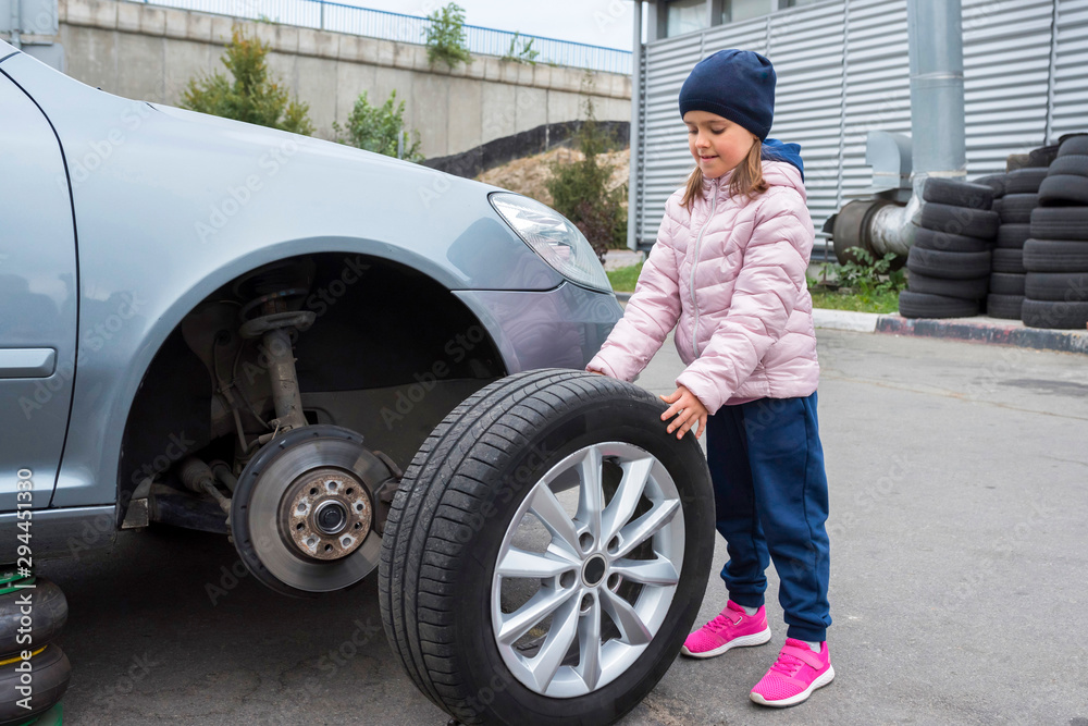 Little girl in a car service, on replacing wheel tires and servicing a vehicle suspension. Auto repair concept. Little girl in a car service, on replacing wheel tires and servicing a vehicle suspension. Auto repair concept.