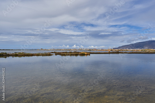 Landscape picture of saltpans in traditional salt production close to sicilian city Trapani in italy with mountain of Erice and Trapani harbour in background. Picture takn in sunny cloudy summer day.