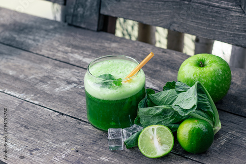 Green apple smoothie in glass and kale leaves on wooden table