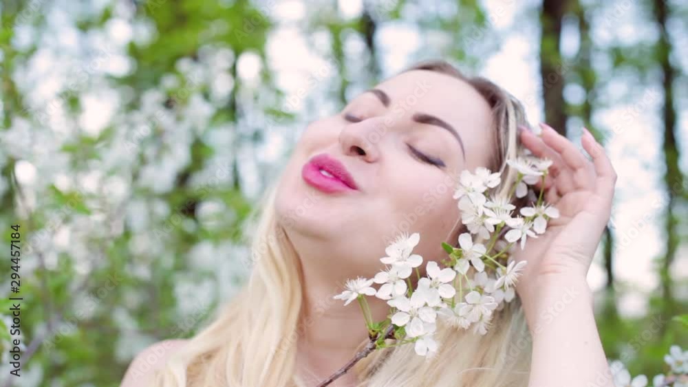 Face of a beautiful blonde woman close-up. She strokes a branch with flower buds in the garden. Face of a beautiful blonde woman close-up. She strokes a branch with flower buds in the garden.