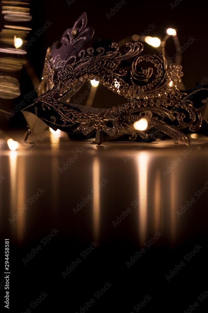 A portrait of a mysterious venetian mask on a wooden table surrounded by lights and their reflection. It is perfect to hide someones identity. - obrazy, fototapety, plakaty 