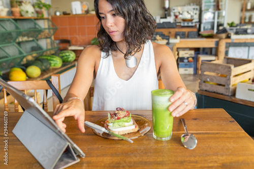 Young woman in organic store, using tablet, eating healthy snack