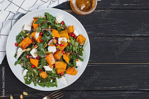 Salad with pumpkin, arugula, feta cheese and pomegranate seeds on black wooden table