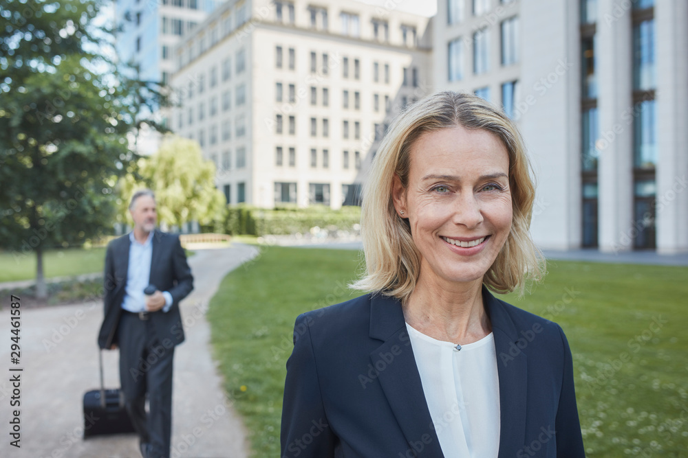 Porrait of smiling blond businesswoman in the city with businessman in background Porrait of smiling blond businesswoman in the city with businessman in background