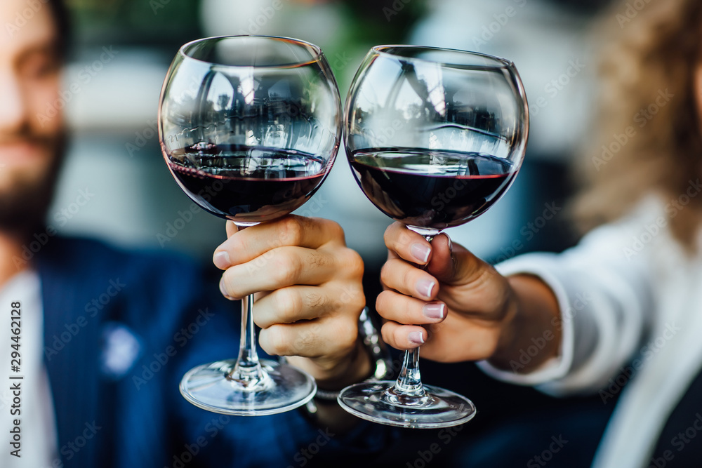 Beautiful young couple with glasses of red wine in luxury restaurant, close up photo.