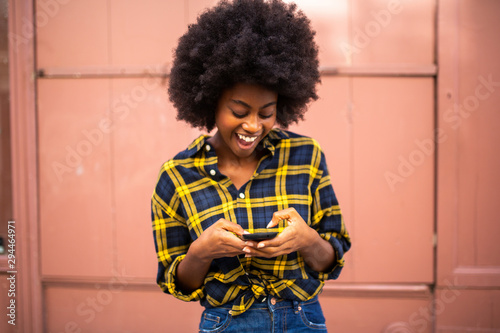 cheerful young black woman laughing and looking at phone