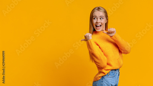 Cheerful cute girl pointing on copy space behing her back