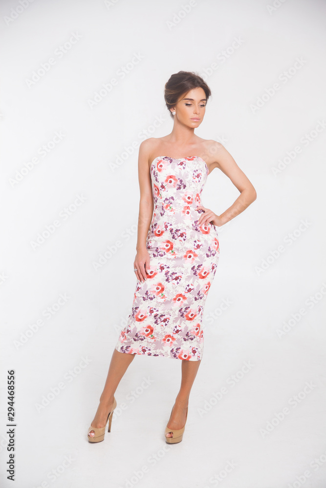 Beautiful elegant young woman with fashion hairstyle and makeup posing on a white background on high heels isolated in a floral dress. Free space for text mockup Beautiful elegant young woman with fashion hairstyle and makeup posing on a white background on high heels isolated in a floral dress. Free space for text mockup