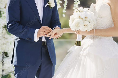 Hands with wedding rings. Modish groom putting a golden ring on the bride's finger during the wedding ceremony. Loving couple, a girl in a wedding dress and handsome man in a stylish blue suit