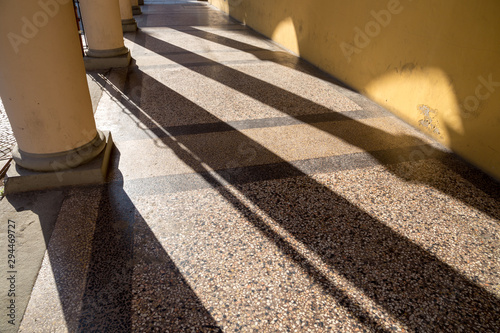 Arched passageway (arcade) in Bologna, Italy: columns are casting long shadows on terrazzo floor and yellow wall.