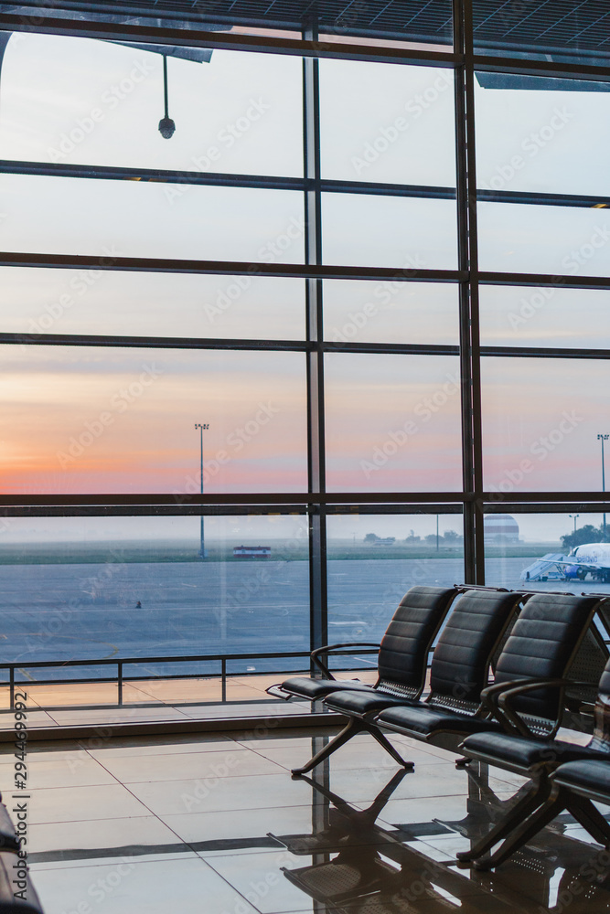Obraz premium View of airport interoir, empty bench chairs in the departure hall during sunrise. Airplane and building background. Travel and transportation concept