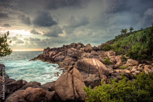 Rocky beach sea lagoon tropical scenery with palm trees and round stones with dramatic sunset sky vibrant colors in Sri Lanka