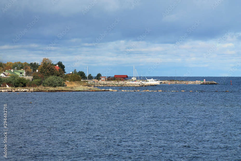 Autumn sea landscape. View of the pier and the village. Cloudy weather, blue sea.