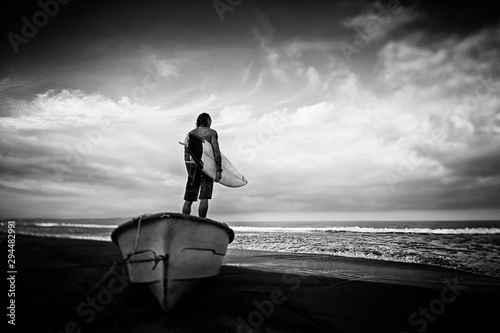 Male surfer with surfboard standing on beached boat, Higuera Blanca, Nayarit, Mexico