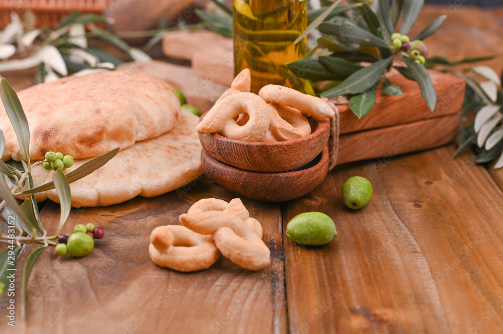 resh and tasty ciabatta on a wooden background. Homemade cakes, olives on fresh branches and oil in a bottle.