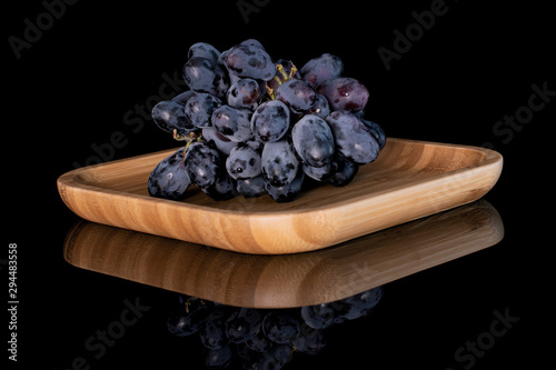 Lot of whole fresh black grape one cluster on wooden square plate isolated on black glass photo