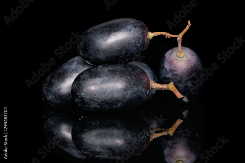 Group of four whole fresh black grape berries isolated on black glass photo