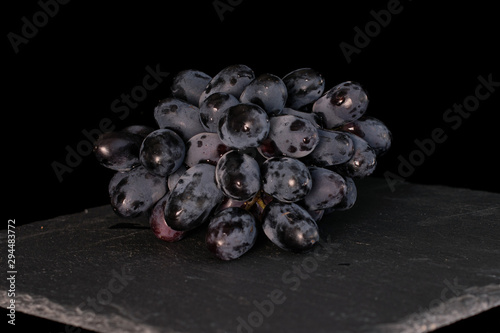 Lot of whole fresh black grape on grey stone isolated on black glass