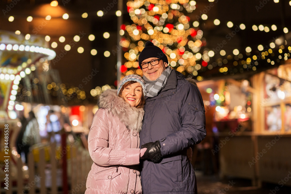 love, winter holidays and people concept - happy senior couple hugging at christmas market on town hall square in tallinn, estonia love, winter holidays and people concept - happy senior couple hugging at christmas market on town hall square in tallinn, estonia