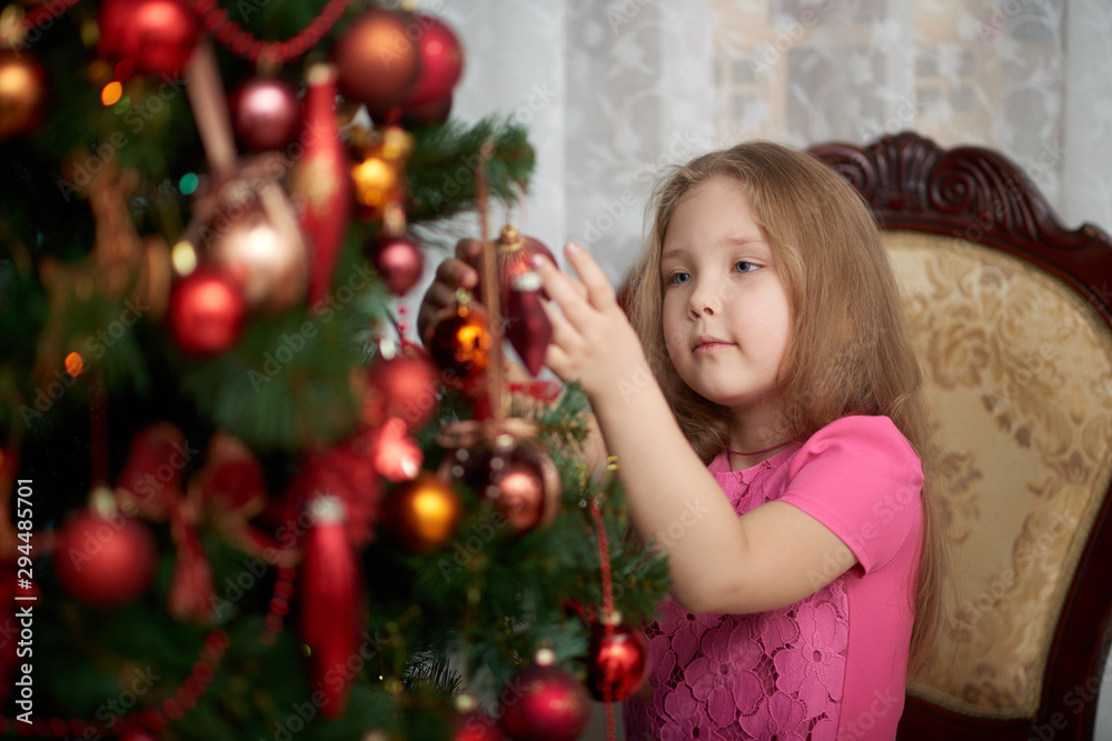 A little girl wearing light pink dress decorating a Christmas tree.