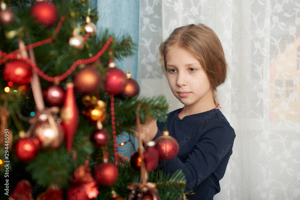 A young girl wearing a blue long sleeve shirt decorating Christmas tree.
