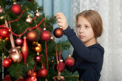 A young girl wearing a blue long sleeve shirt decorating Christmas tree. © shabbydatwin