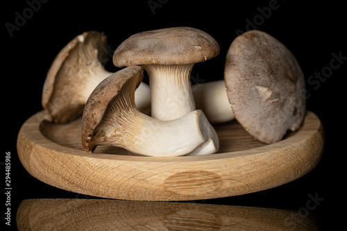 Group of four whole fresh creamy king trumpet mushroom on bamboo plate isolated on black glass