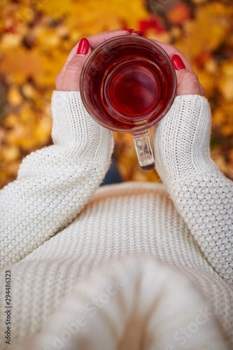 Woman with red nails holds in her hands an autumn cup close-up