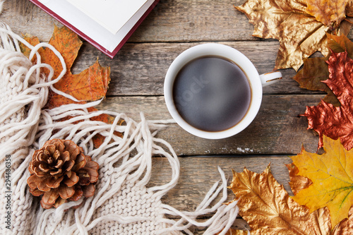 Autumn layout  hot coffee  book  golden autumn leaves  knitted sweater  plaid on a wooden table. Cozy autumn mood in October  November