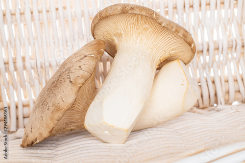 Group of two whole raw fresh creamy king trumpet mushroom with braided rattan behind
