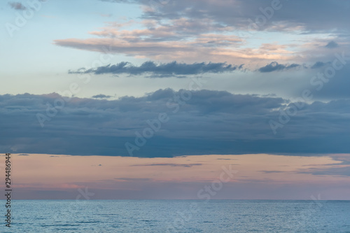 Blue, pink, white clouds over the blue sea at the sunset