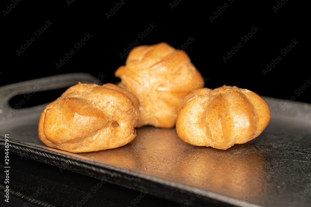 Group of three whole baked golden profiterole on tray isolated on black glass