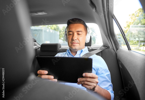transport, business and technology concept - male passenger or businessman with wireless headphones using tablet pc computer on back seat of taxi car © Syda Productions
