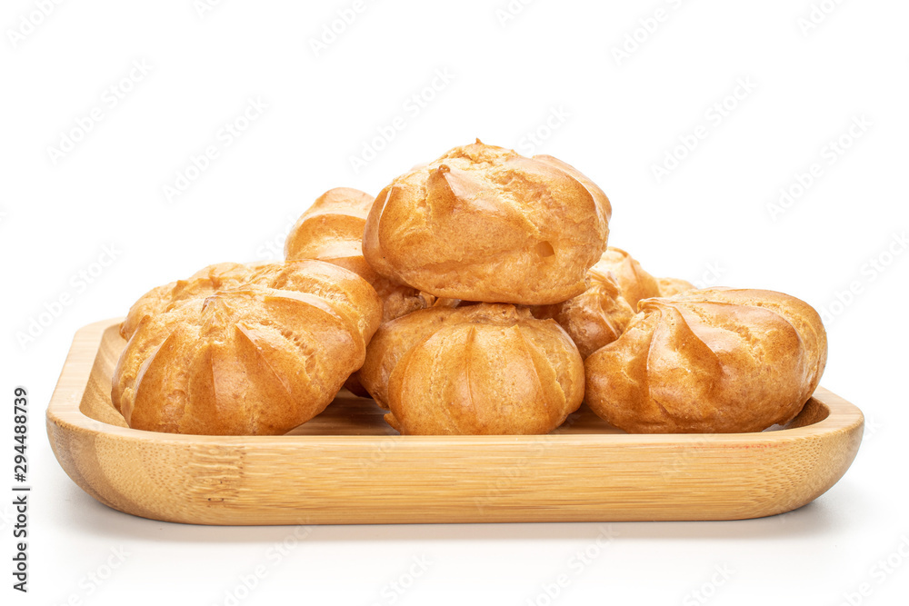Lot of whole baked golden profiterole on wooden square plate isolated on white background