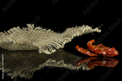 Group of two slices of dry red cherry tomato with jute cloth isolated on black glass