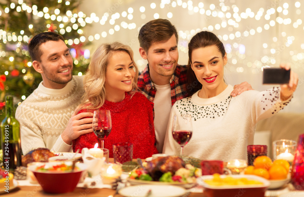 holidays and celebration concept - happy friends taking selfie by smartphone at home christmas dinner