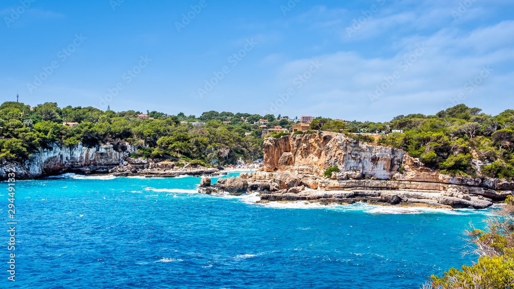 Houses on cliffs around beautiful beach, Cala Llombards in Mallorca, turquoise water and blue sky, Balearic Island, Spain