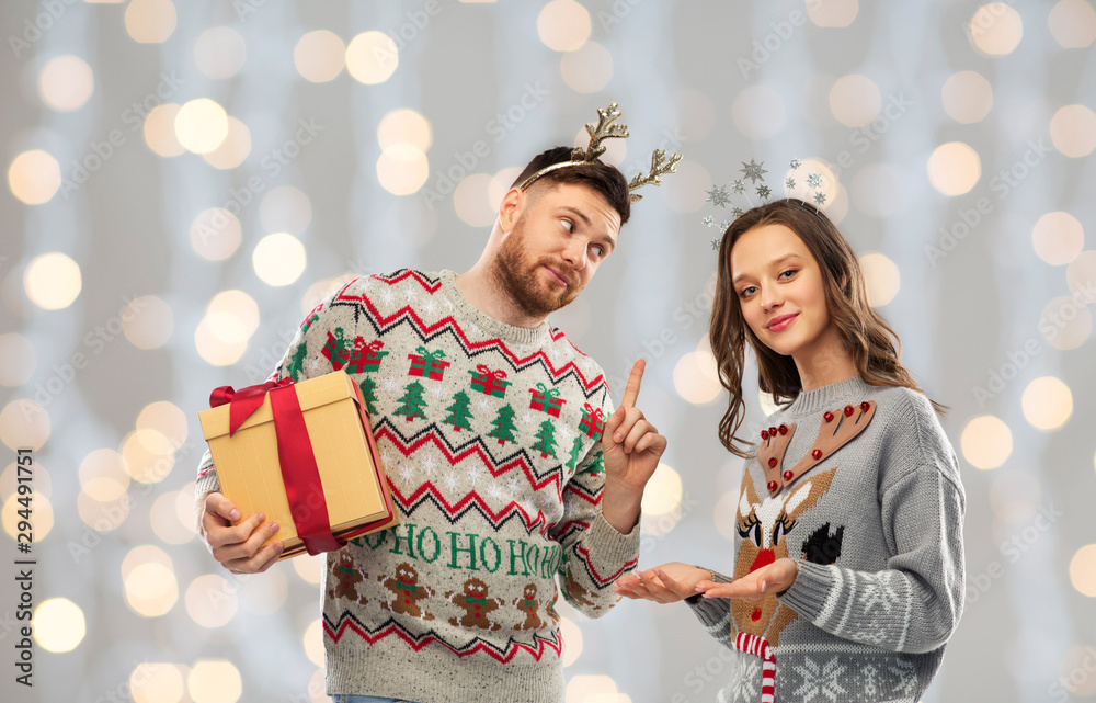 people and holidays concept - portrait of happy couple with christmas gift at ugly sweater party over festive lights background people and holidays concept - portrait of happy couple with christmas gift at ugly sweater party over festive lights background